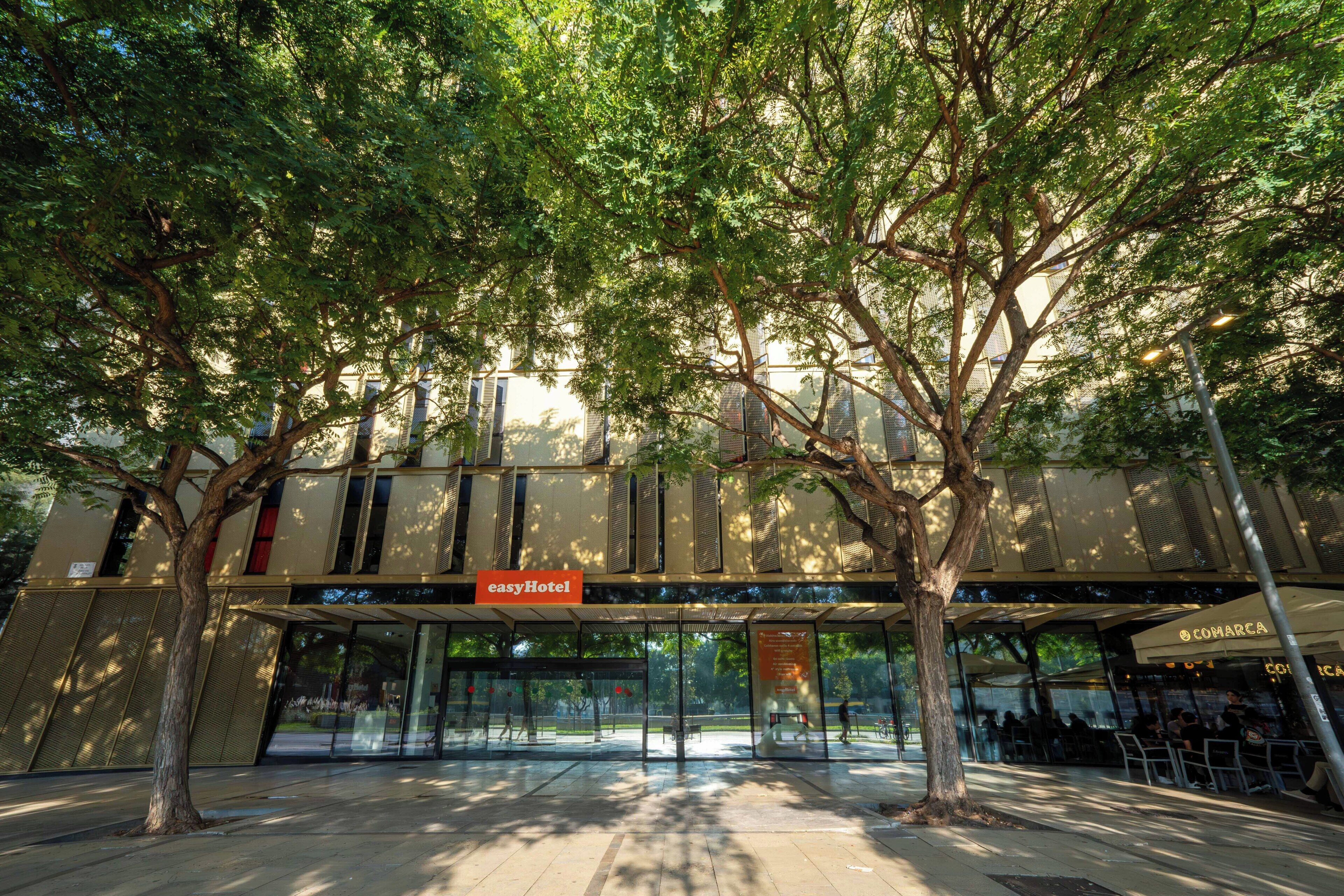 Een hotelingang met een glazen gevel, een bord met 'easyHotel' en een nabijgelegen restaurant genaamd 'COMARCA'.