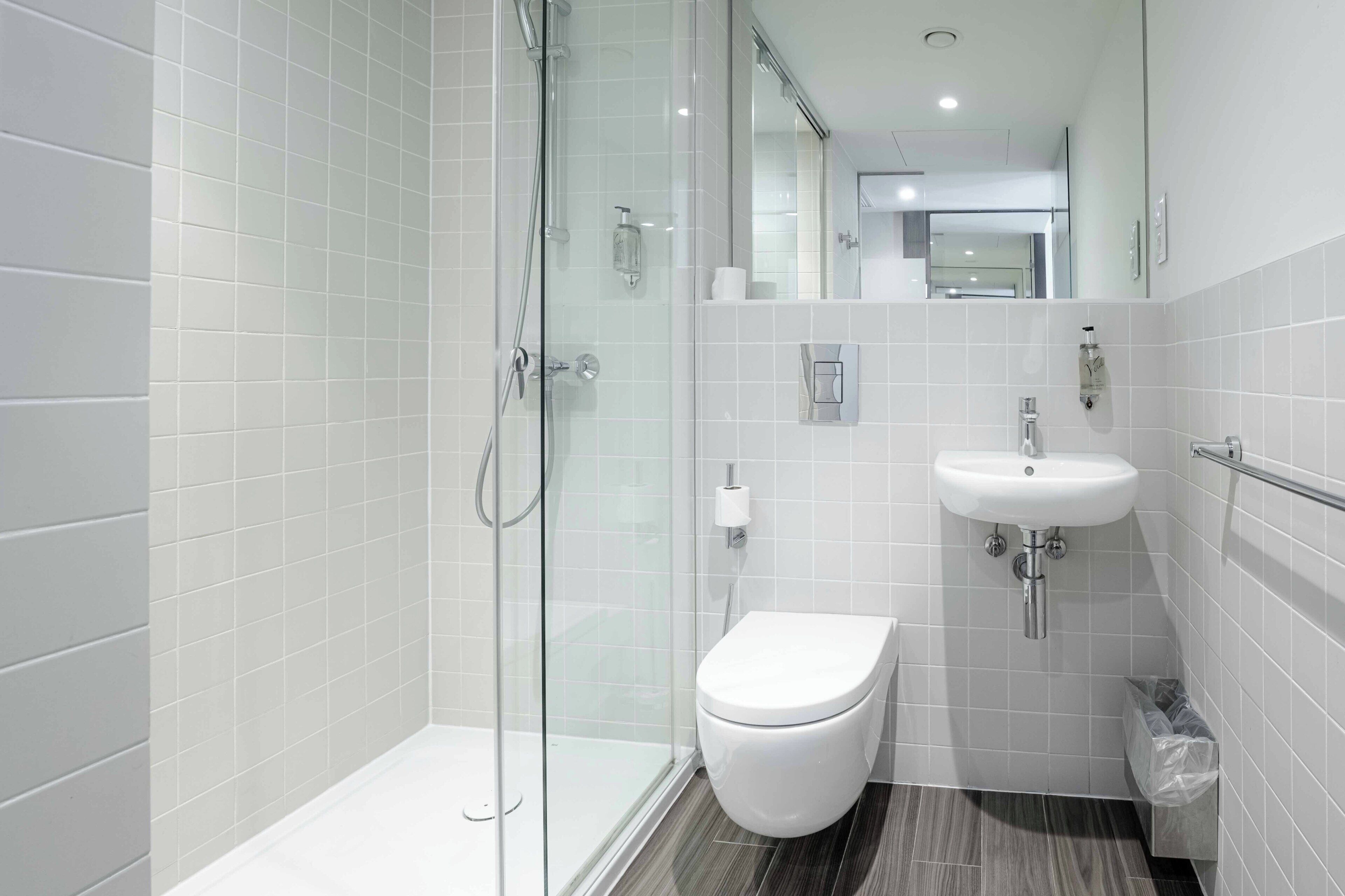 A modern bathroom with a glass shower enclosure, a white toilet, and a sink with a mirror above it.