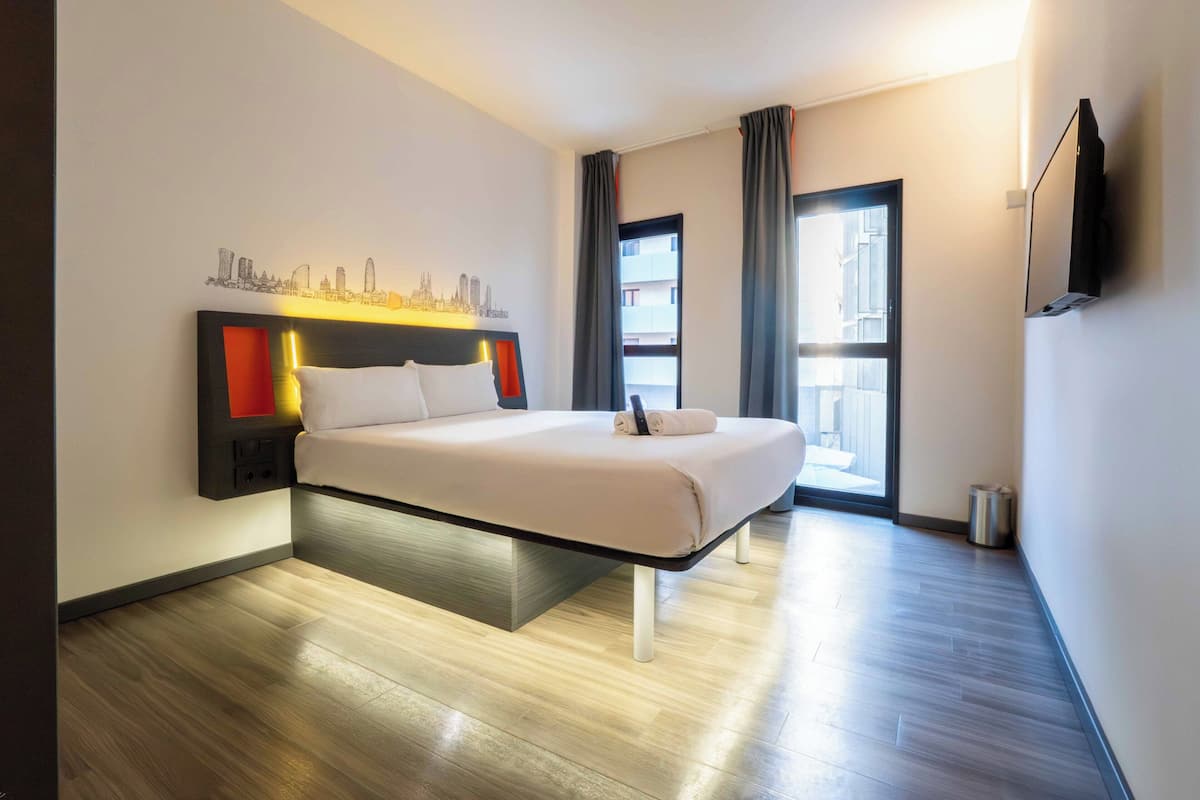 Una habitación de hotel moderna con una cama, una obra de arte urbana, un televisor y una ventana con cortinas.
