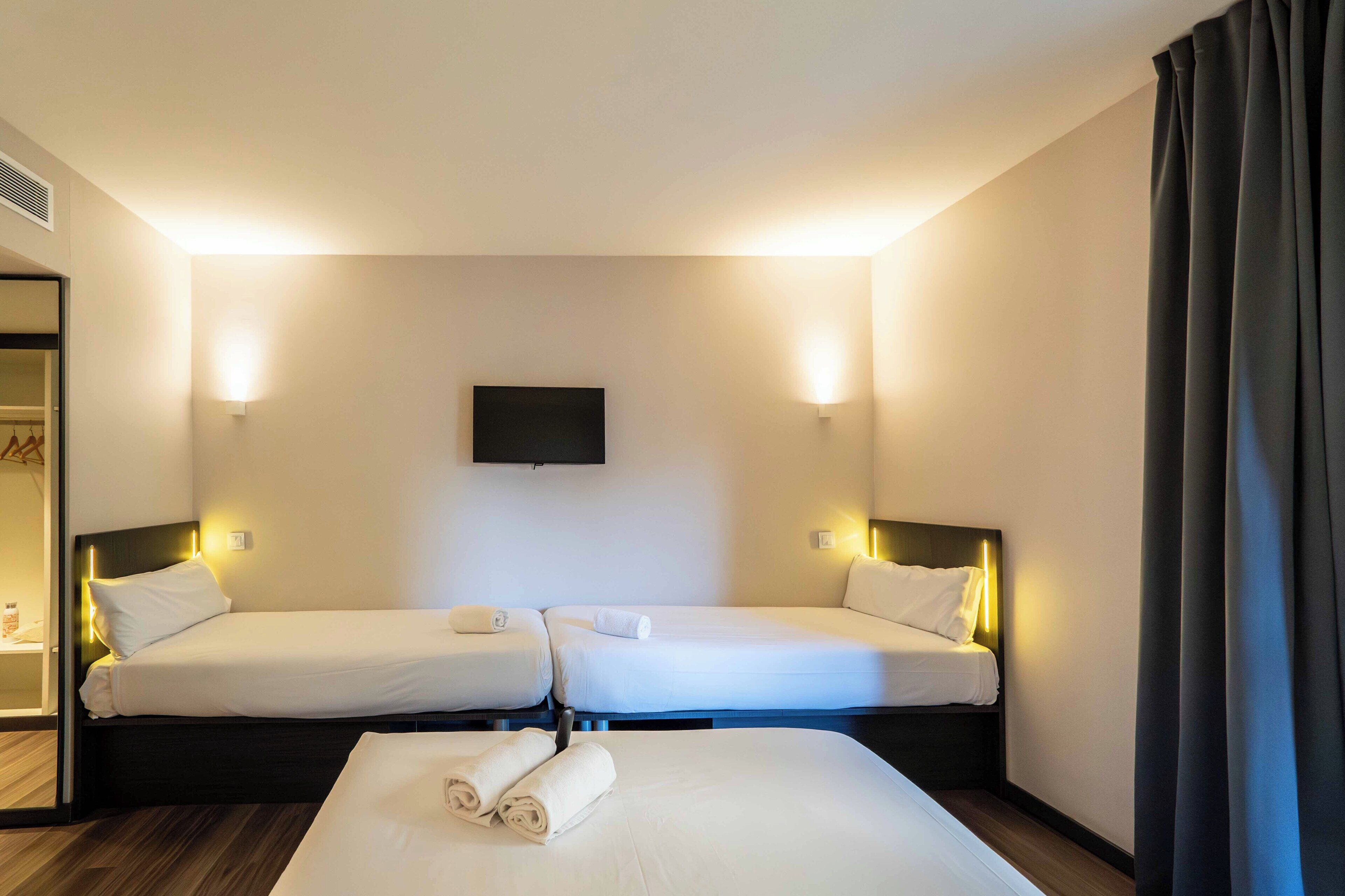 Ein Hotelzimmer mit zwei Betten, einem an der Wand montierten Fernseher und einem Kleiderschrank.