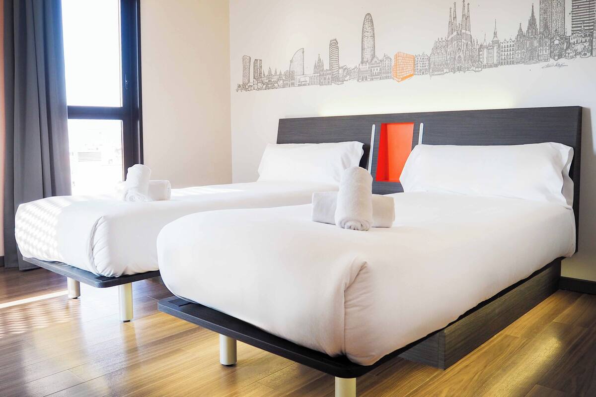 Habitación de hotel con dos camas, un cuadro de arte urbano en la pared y suelo de madera.