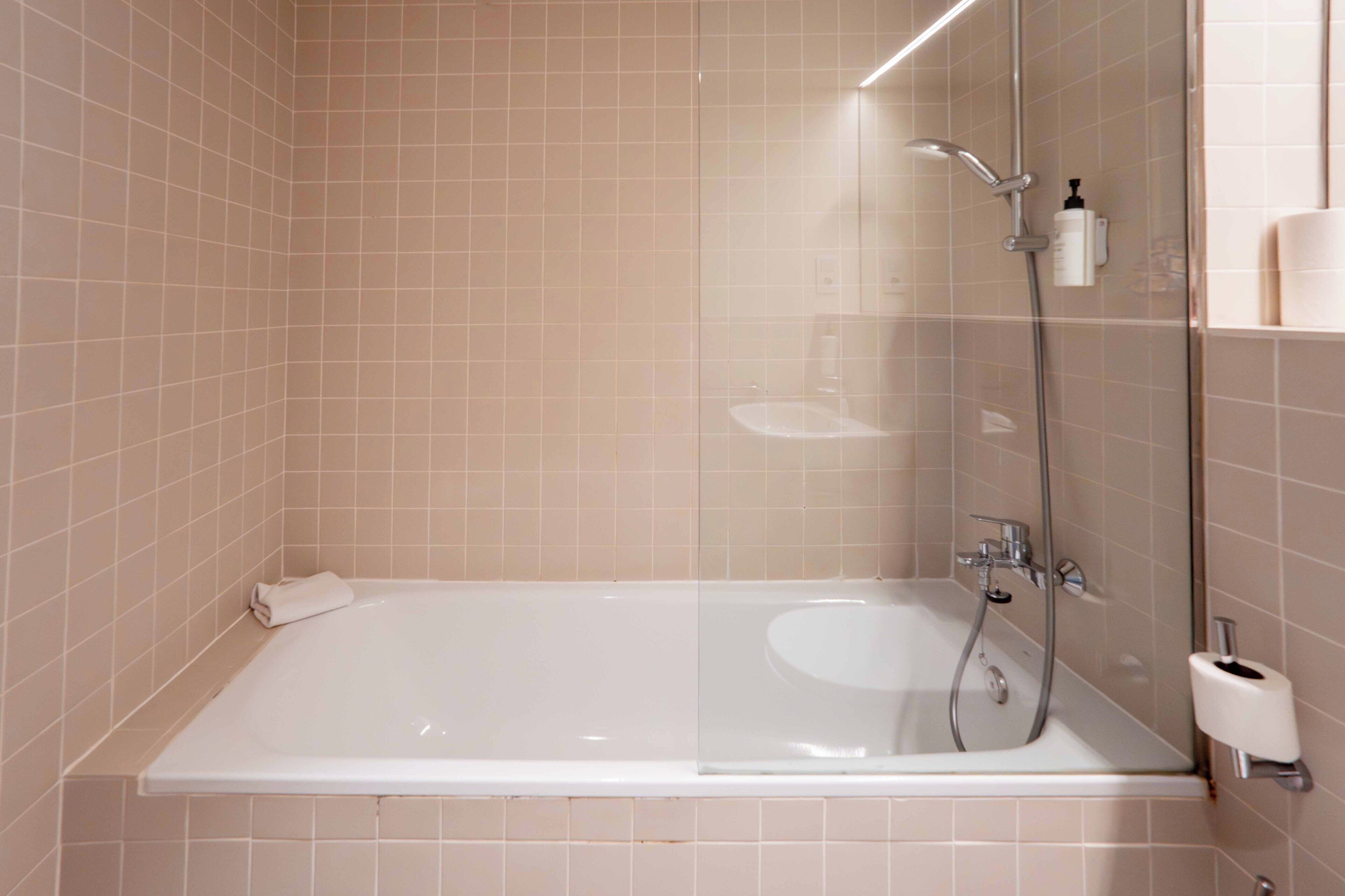 Un baño moderno con ducha envuelta en vidrio, una bañera blanca y un dispensador de papel higiénico a la vista.