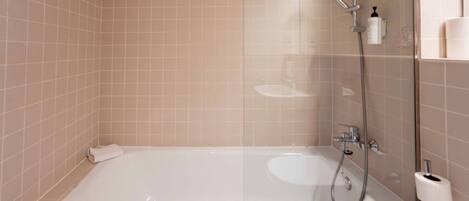Un baño moderno con ducha envuelta en vidrio, una bañera blanca y un dispensador de papel higiénico a la vista.