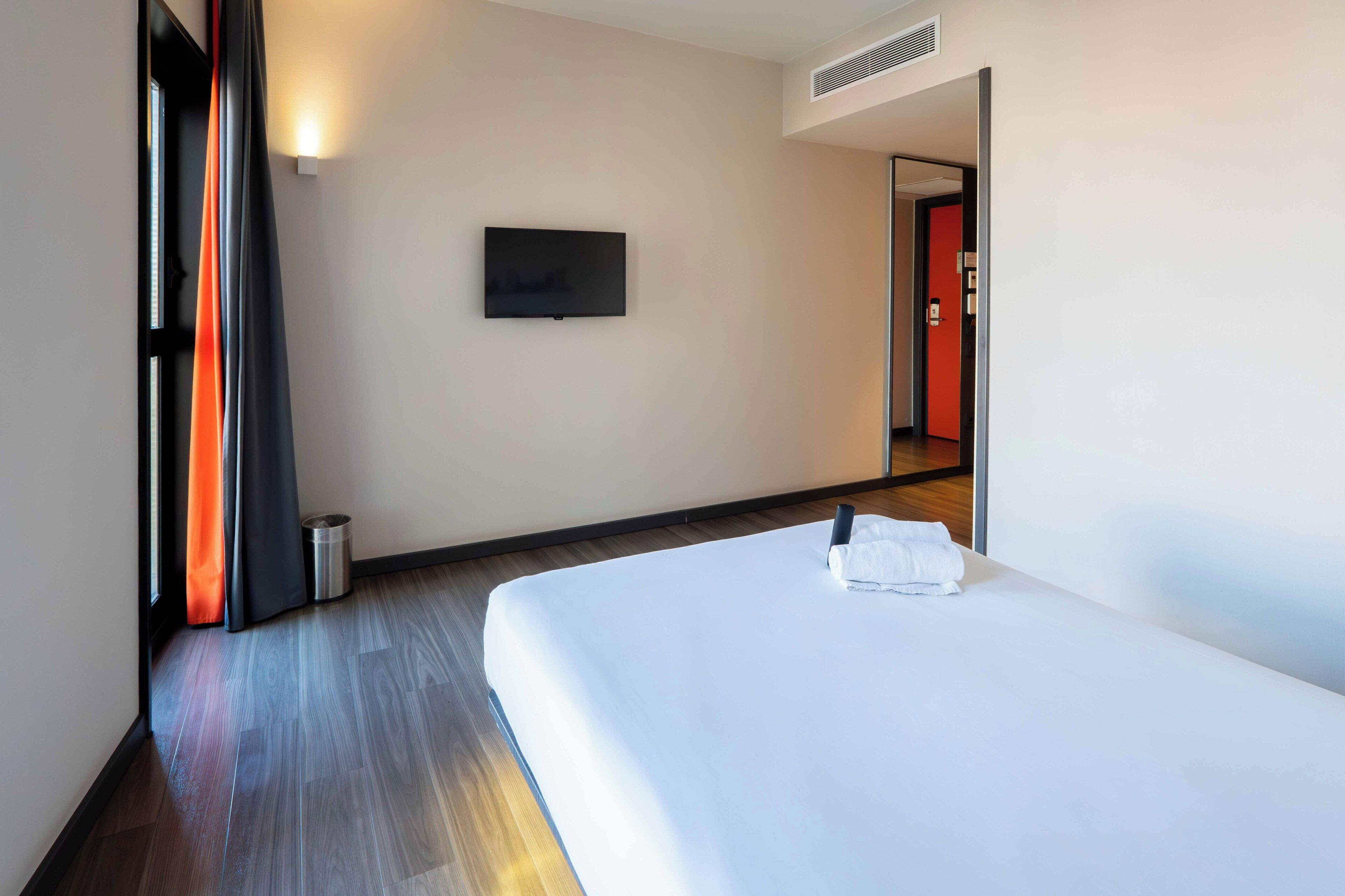Een hotelkamer met een bed, een aan de muur bevestigde televisie en een deur die naar een andere kamer leidt.