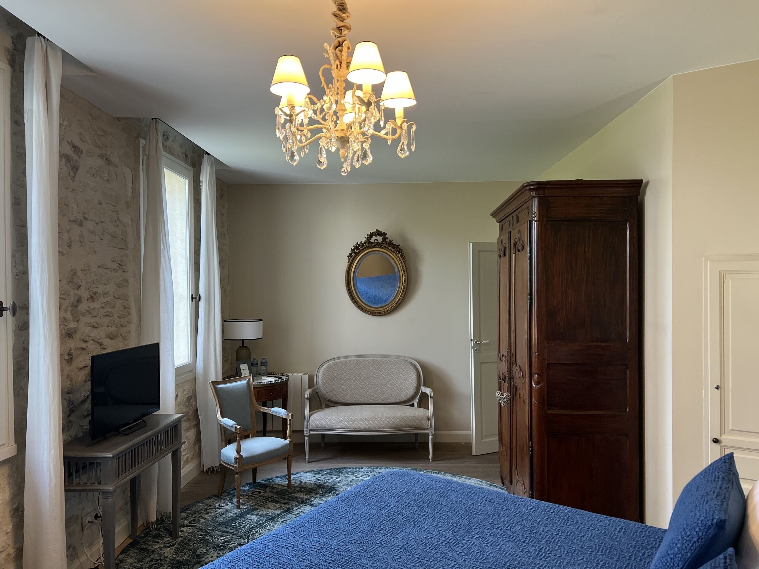 Een slaapkamer met een bed, een televisie, een stoel, een kledingkast, een spiegel en een kroonluchter.