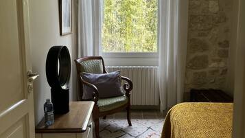 A room with a bed, a chair, a radiator, a window with curtains, a door, and a wall with a stone pattern.