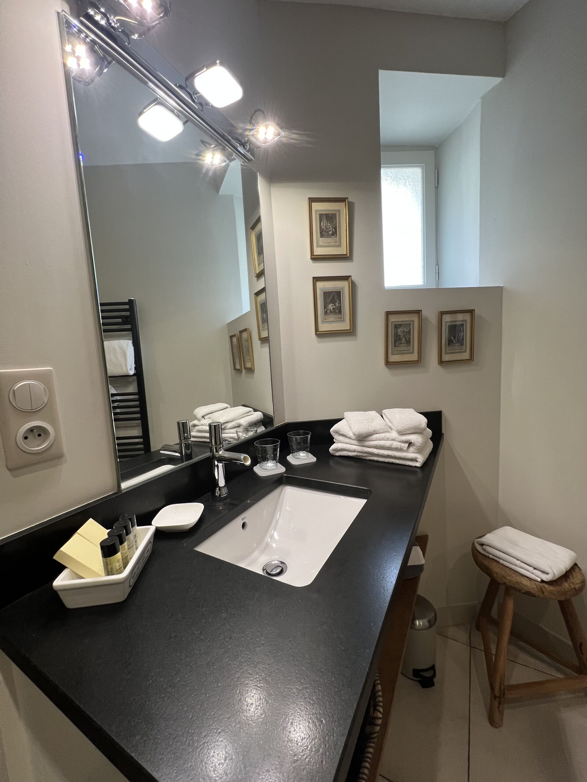 Un baño moderno con encimera negra, un espejo grande y cuadros en la pared.