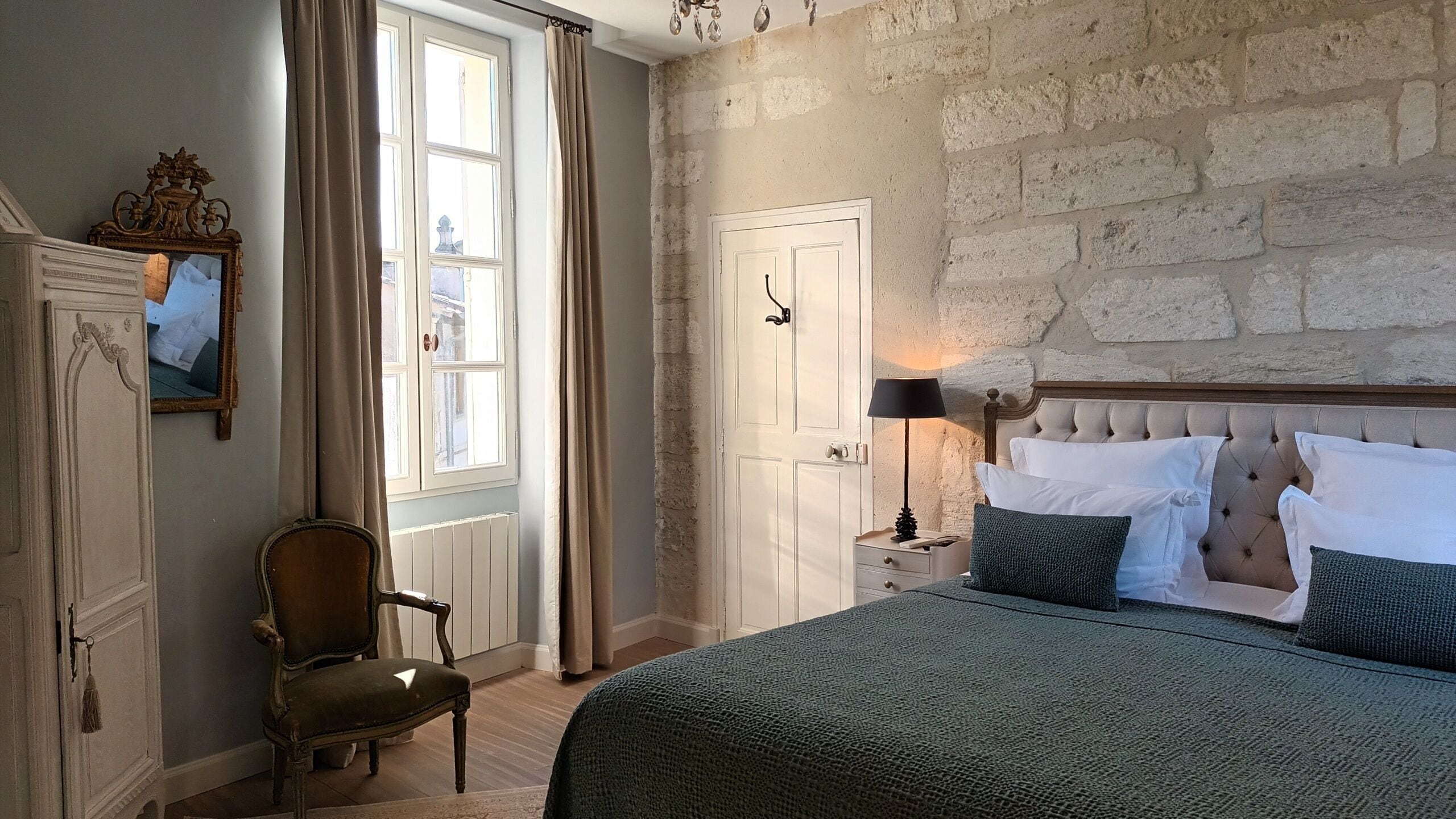A bedroom with a large bed, a nightstand with a lamp, a chair, and a wardrobe.
