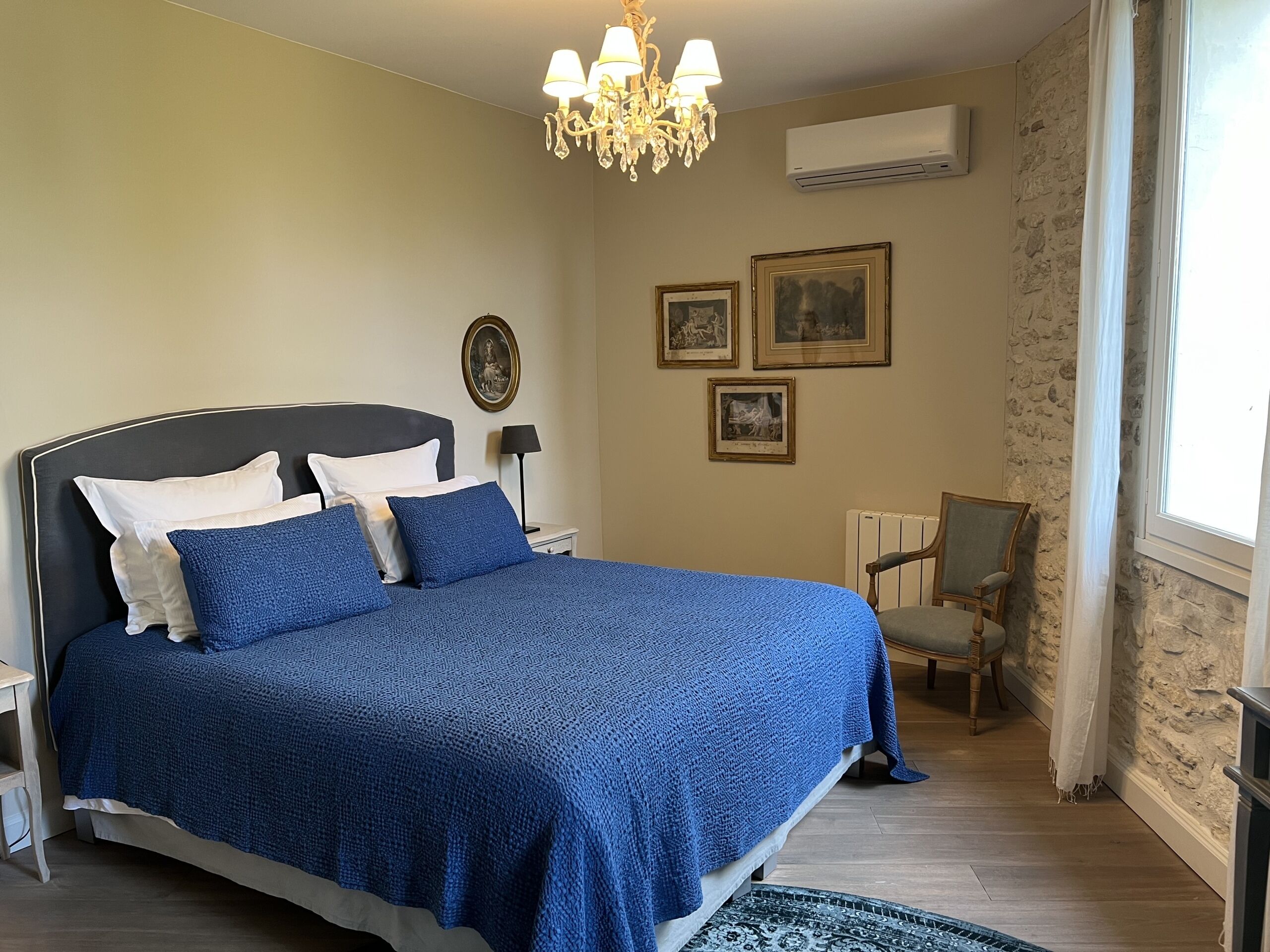 Un dormitorio con una cama grande, una silla, una araña y cuadros en la pared.