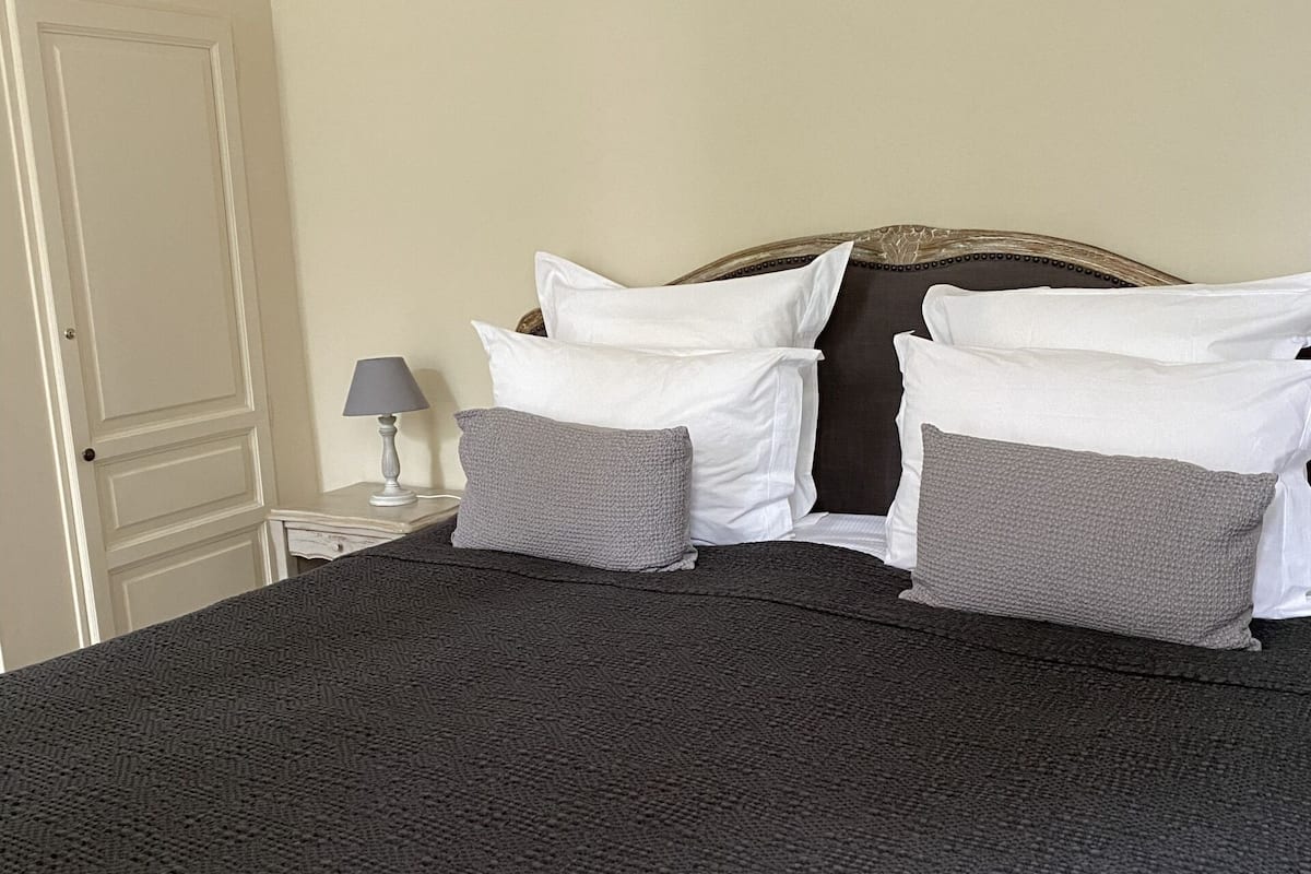 Een bed met een donkere, structuurrijke spreideken, witte kussens en een hoofdbord.