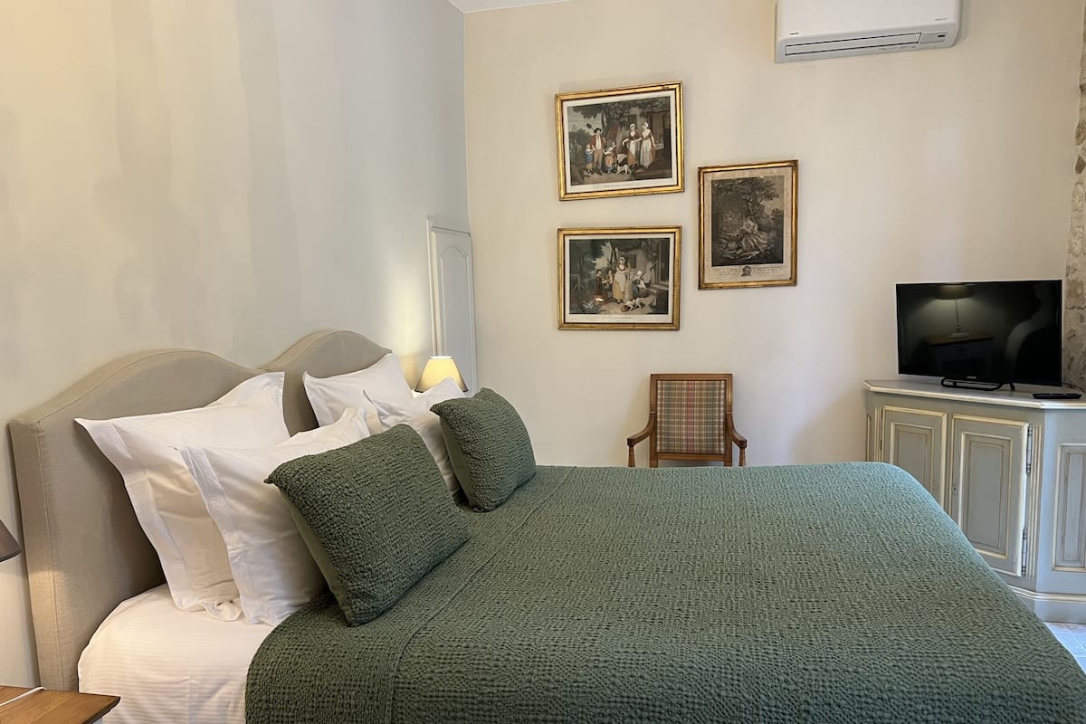 Een net opgemaakt bed met groene beddengoed, een televisie op een kastje, en drie ingelijste foto’s aan de muur.