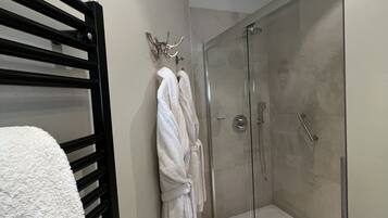 Un baño con ducha envuelta en vidrio, un perchero negro y una bata blanca colgada en la pared.