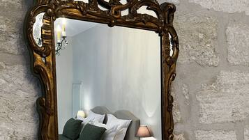 A mirror with an ornate frame reflecting a bedroom with a bed, pillows, a nightstand, and a lamp.