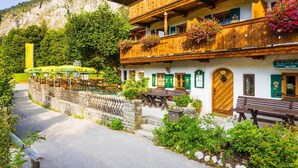 Un edificio de madera tradicional con balcones, un muro de piedra y montañas al fondo.