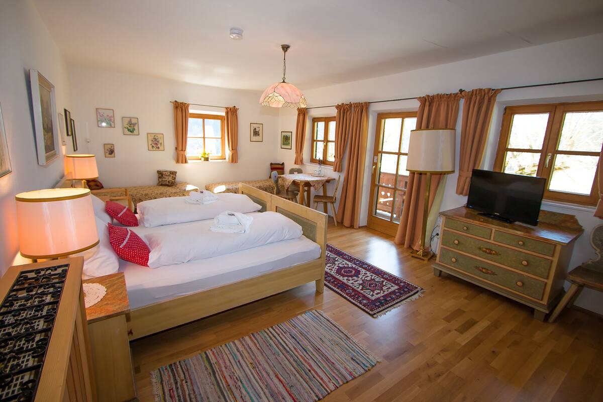 A bedroom with a bed, bedside table, lamp, dresser, TV, and a small table with chairs.