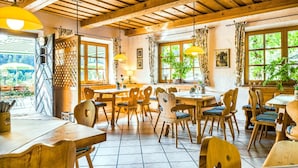 Un comedor rústico con mesas y sillas de madera, ventanas grandes con cortinas e iluminación colgante.
