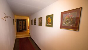 Un pasillo con alfombra roja, cuadros con motivos florales en las paredes y una puerta al final.