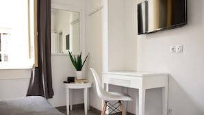 A hotel room with a bed, a desk, a chair, a potted plant, a mirror, and a TV on the wall. - Hostal Guestped (Madrid)