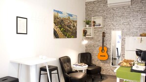A compact living space with a white table, two black chairs, a guitar, and a small kitchenette. - Hostal Guestped (Madrid)
