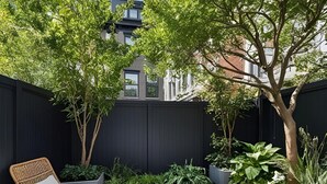 A patio area with two wicker chairs, a black fence, and various plants.