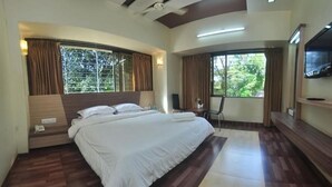 A bedroom with a large bed, a flat-screen TV mounted on the wall, and a window with curtains.