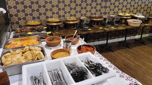 A buffet with various dishes and utensils, including bowls of food, trays of snacks, and a patterned wall in the background.