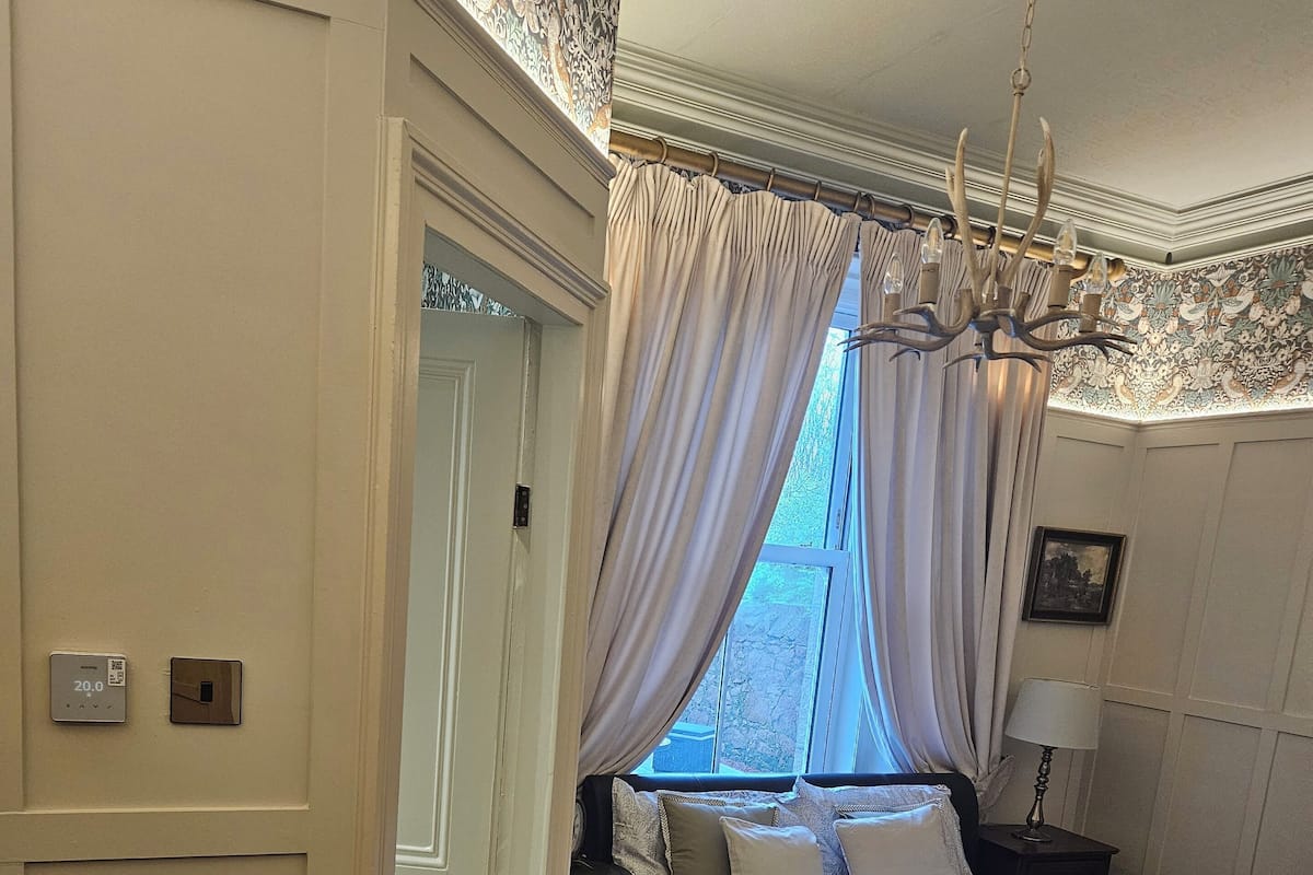 A bedroom with a large bed, a nightstand, a lamp, and a window with curtains.