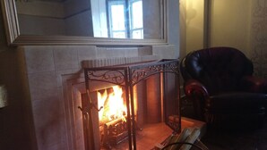 Une cheminée avec un feu, un fauteuil et un miroir au-dessus.