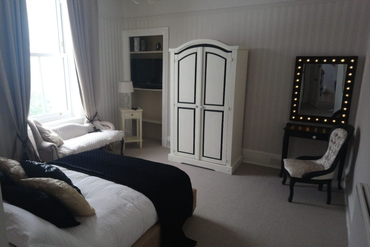 A bedroom with a bed, a vanity with a mirror, a chair, and a wardrobe.