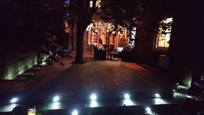 An outdoor area with a wooden structure, possibly a patio or lounge, surrounded by trees and illuminated by overhead lights. - Trinity Boutique B&B (Peterhead)