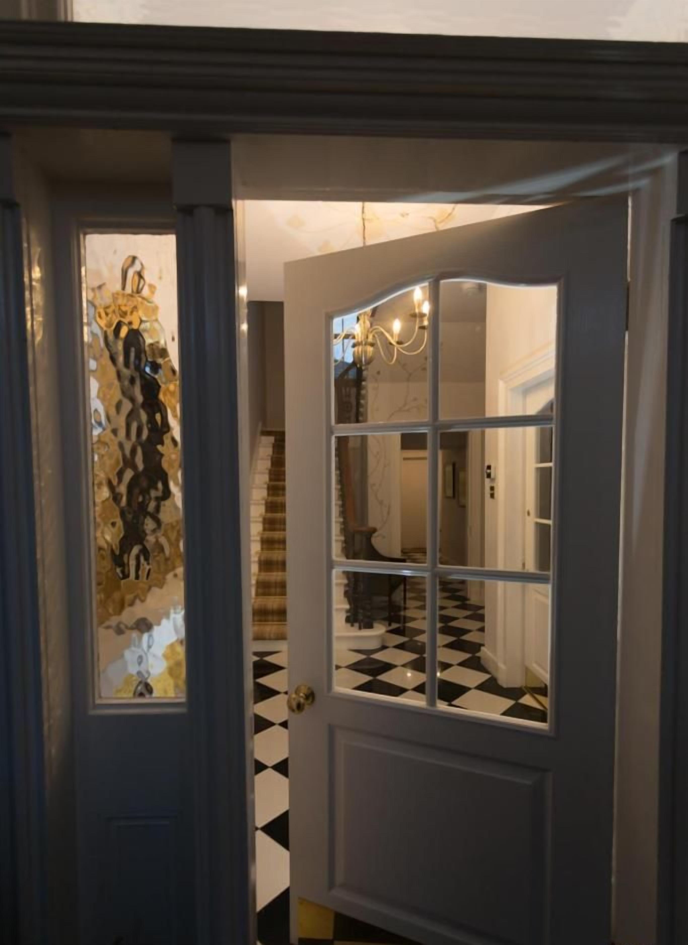 A hallway with a black and white checkered floor, a white door with glass panels, and a staircase in the background.