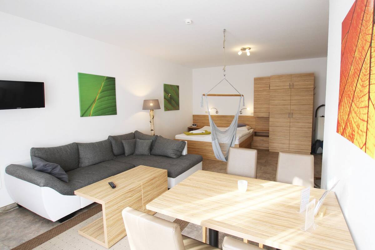 A modern living room with a grey sectional sofa, a wooden dining table, and a hanging chair.