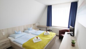 A hotel room with a bed, a desk, a chair, a TV, and a window with curtains. - grünblau Vitalpension (Rostock)