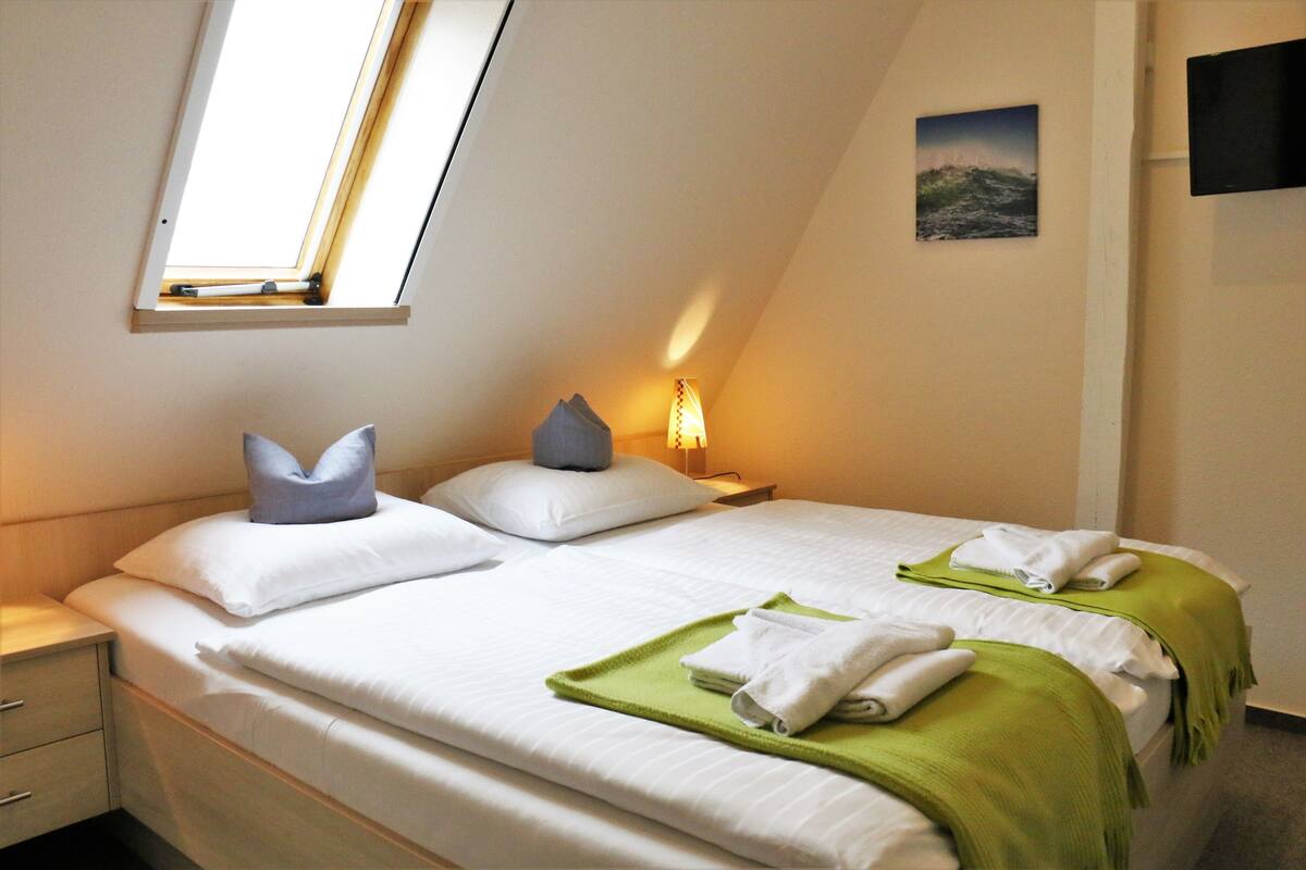 A neatly made bed with pillows, a green towel, and a painting on the wall.