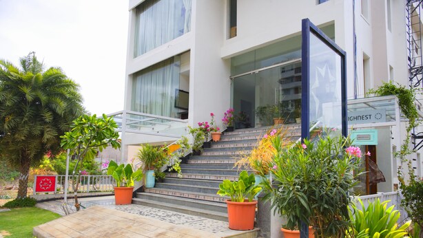 Un edificio moderno con una escalera que lleva a la entrada, rodeado de plantas en macetas y un pequeño jardín.