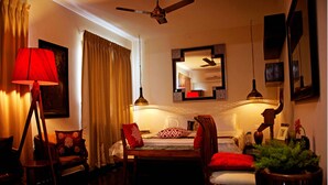 Habitación de hotel con cama, escritorio, silla, lámpara, espejo y ventilador de techo.