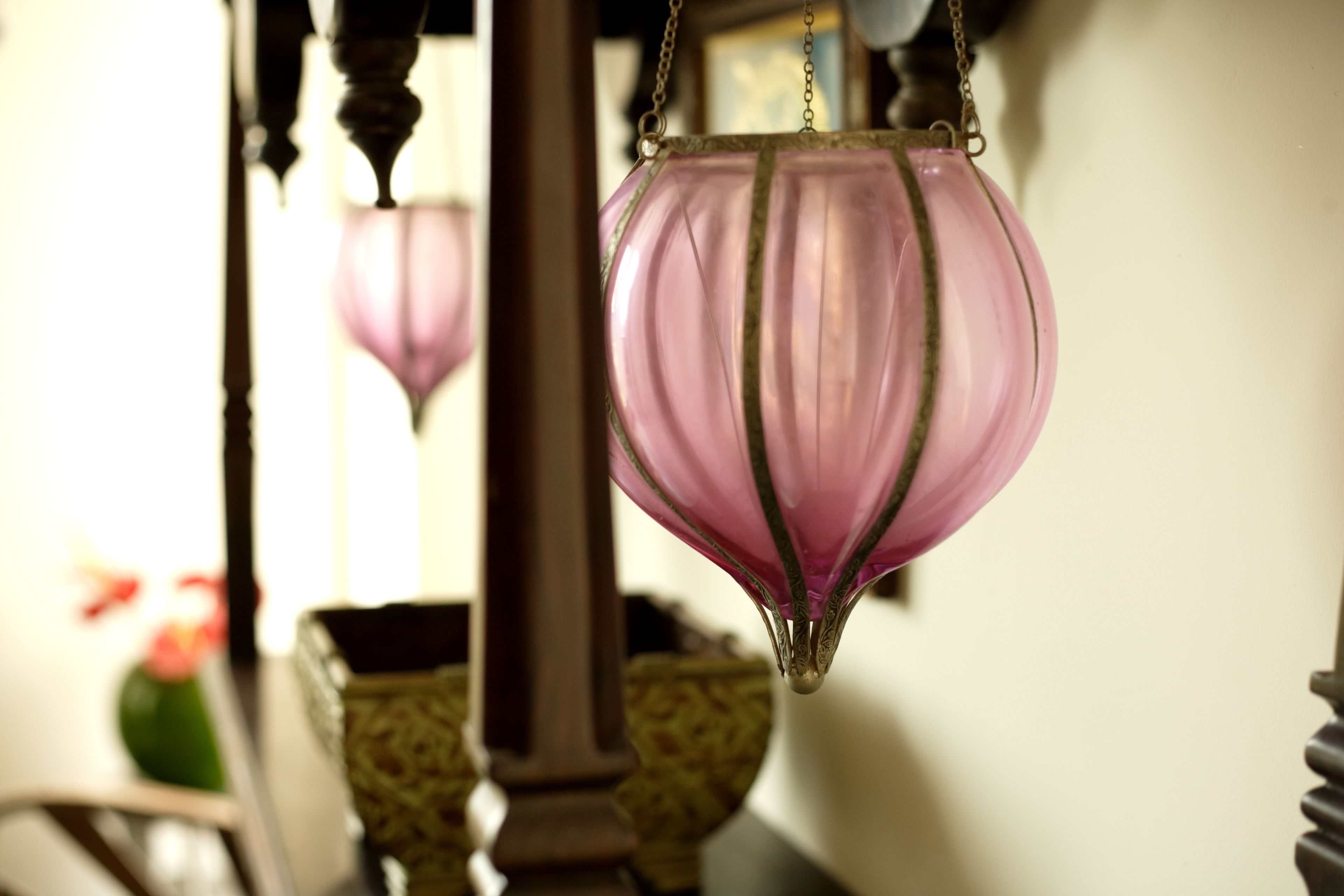 A hanging pink lantern with a chain, a wooden column, and a patterned cushion in the background.