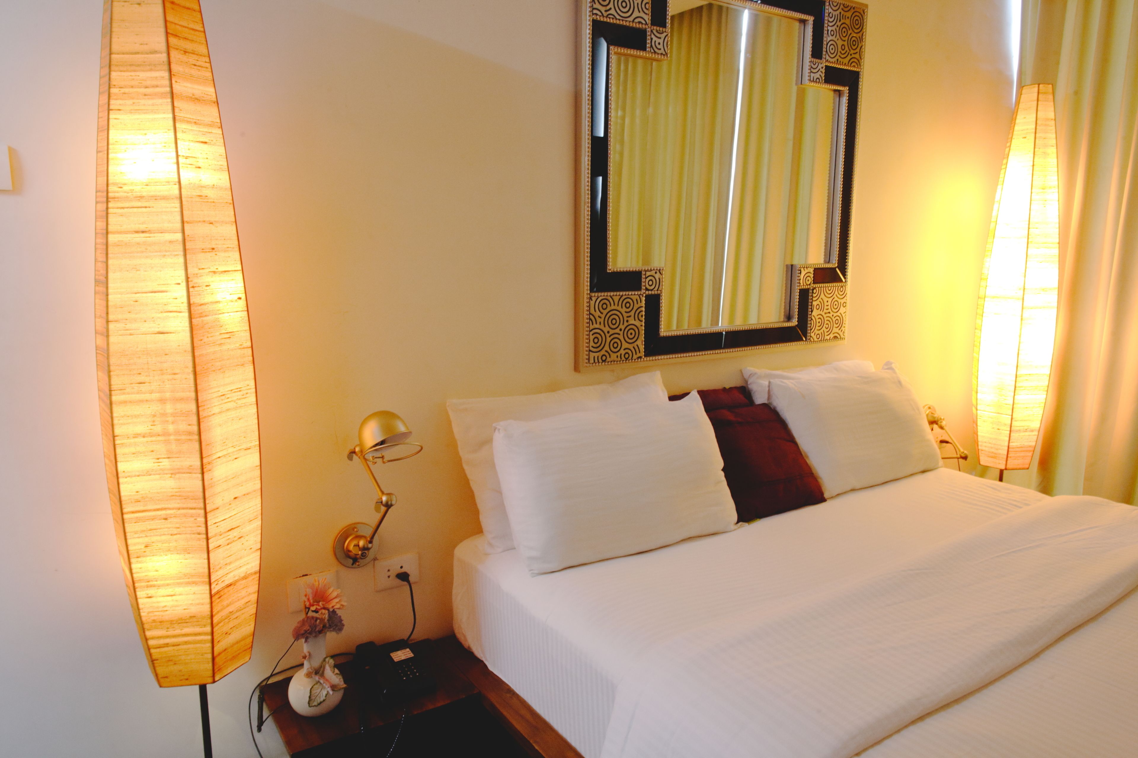 Een hotelkamer met een groot bed, een nachtkastje met een lamp, een spiegel en een wandlamp.