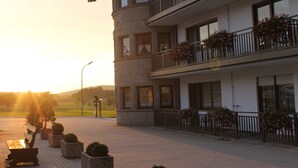 A multi-story building with balconies adorned with flowers, a paved area in front, and a sunset in the background. - Landhotel Kastanienhof (Georgenberg)