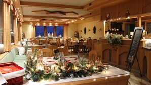 A dining area with a Christmas tree centerpiece, wooden furniture, and a view of the outside. - Landhotel Kastanienhof (Georgenberg)