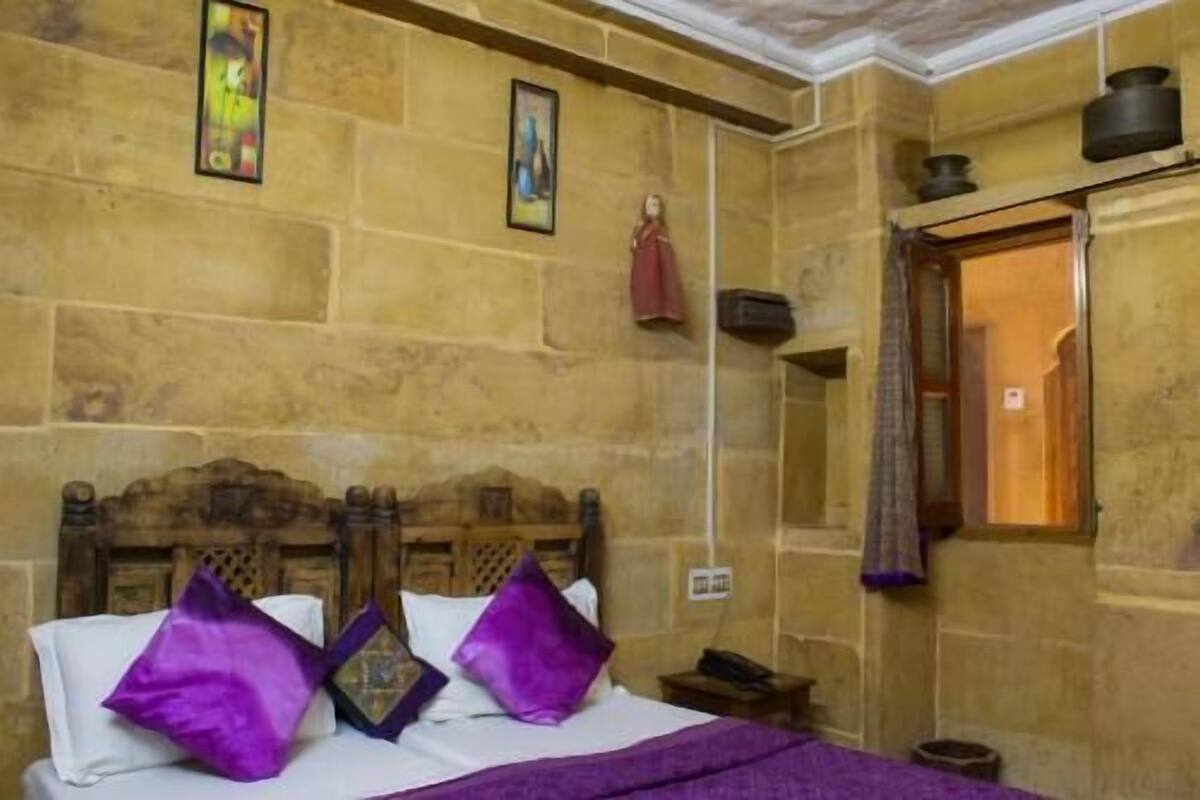A room with a stone wall, a wooden bed with purple pillows, a nightstand, and a window with a curtain.