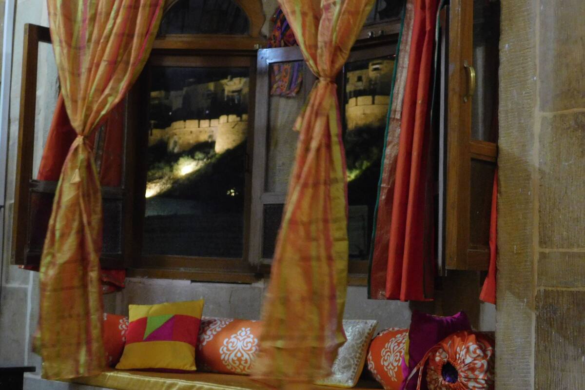 A room with a window, curtains, and a bench with cushions.