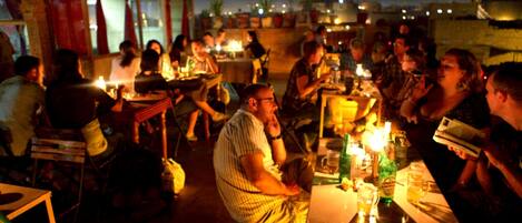 An outdoor dining area with tables and chairs, people sitting and eating, and a view of the city skyline in the background.