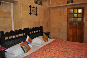 A room with a bed, a wooden door with glass panels, and stone walls. - Hotel Shahi Palace (Jaisalmer)
