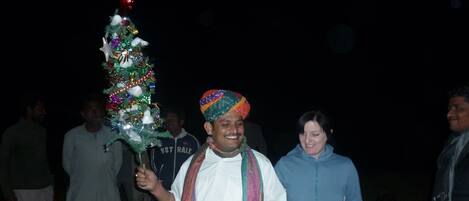 A group of people outdoors at night, some holding a decorated Christmas tree.