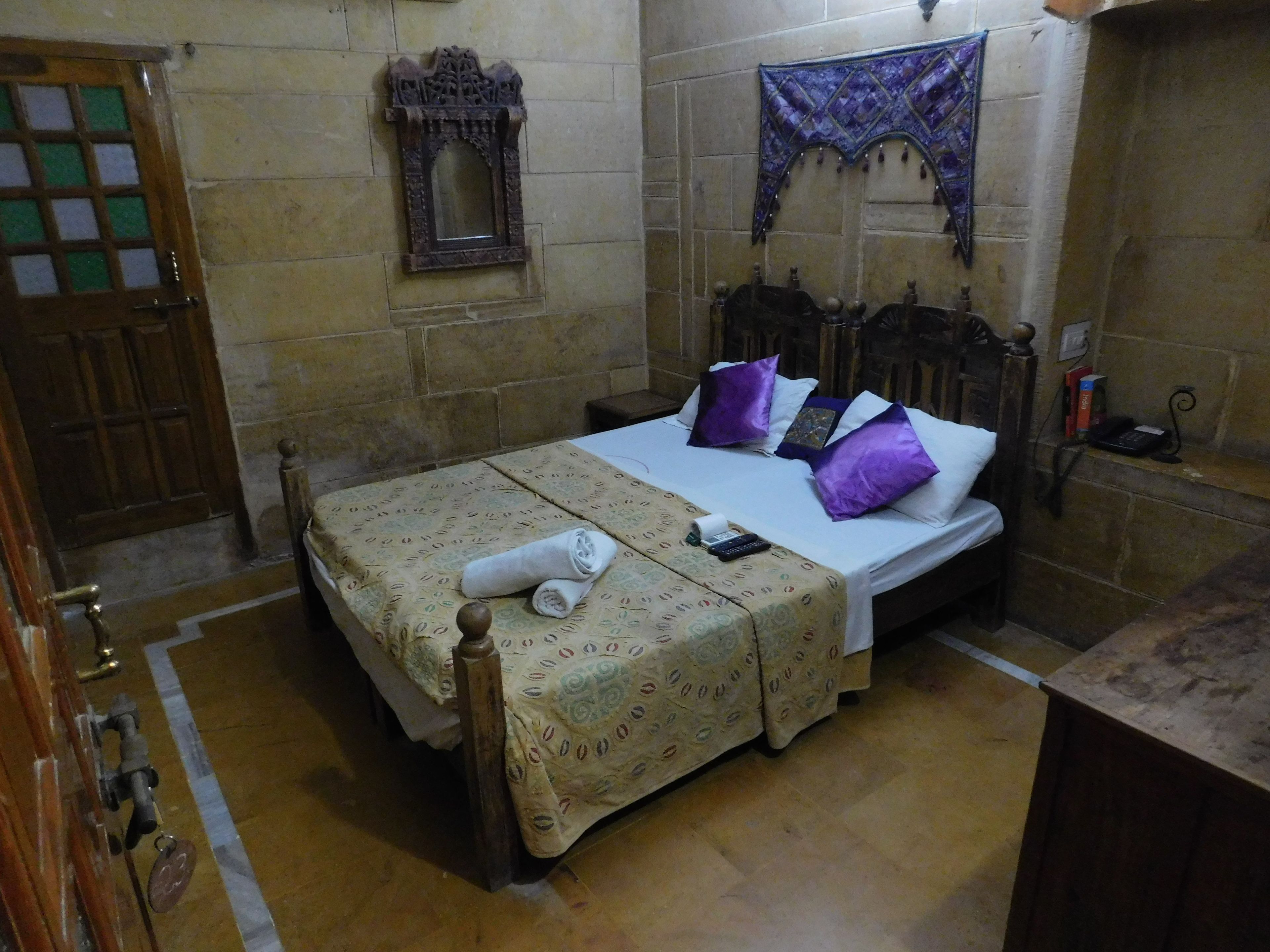 A room with a bed, a wooden door, a mirror, and a wall-mounted tapestry.