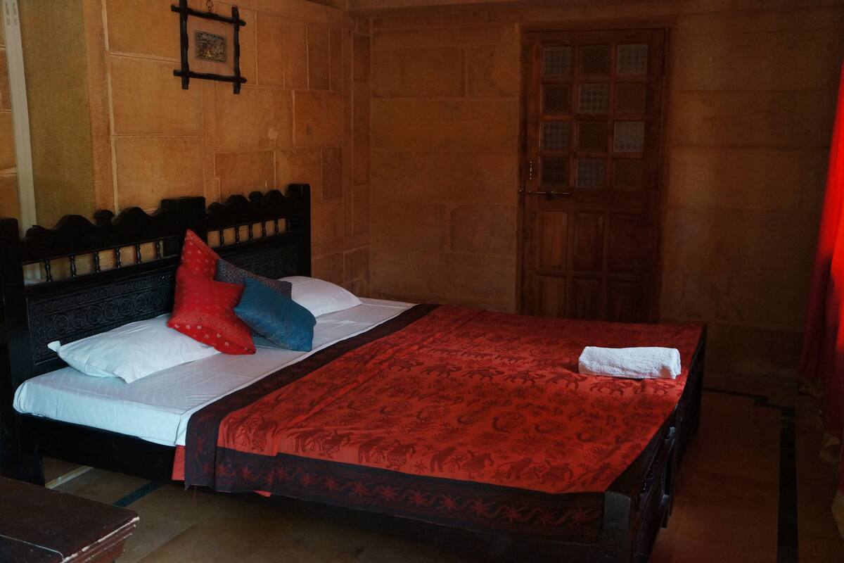 A bed with a wooden headboard, a red patterned bedspread, and pillows in red, blue, and white.