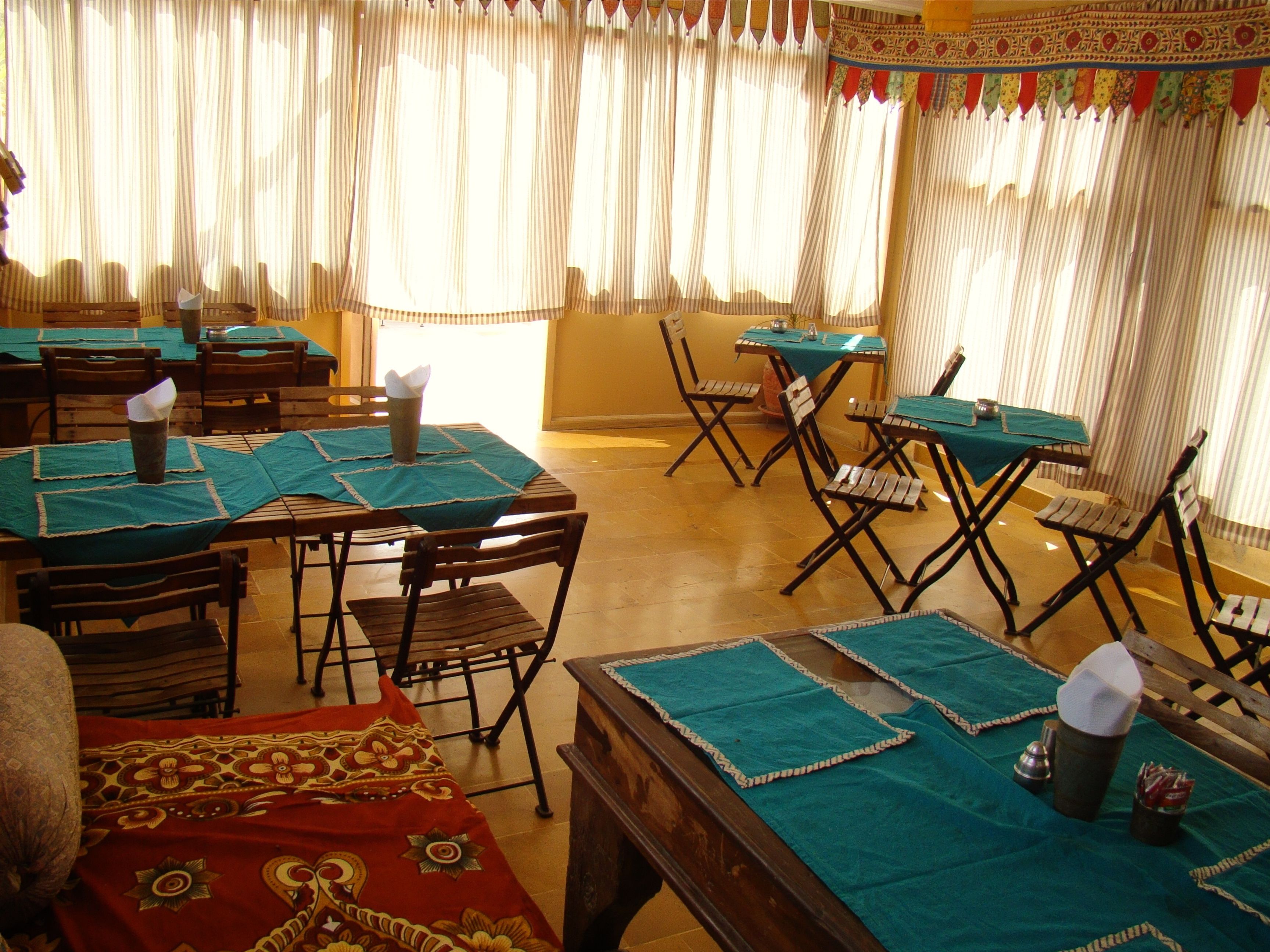 A restaurant with tables covered in green tablecloths, wooden chairs, and a patterned red carpet.