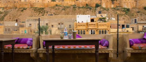 A traditional courtyard with stone benches and tables, surrounded by historic buildings with a fortified appearance.
