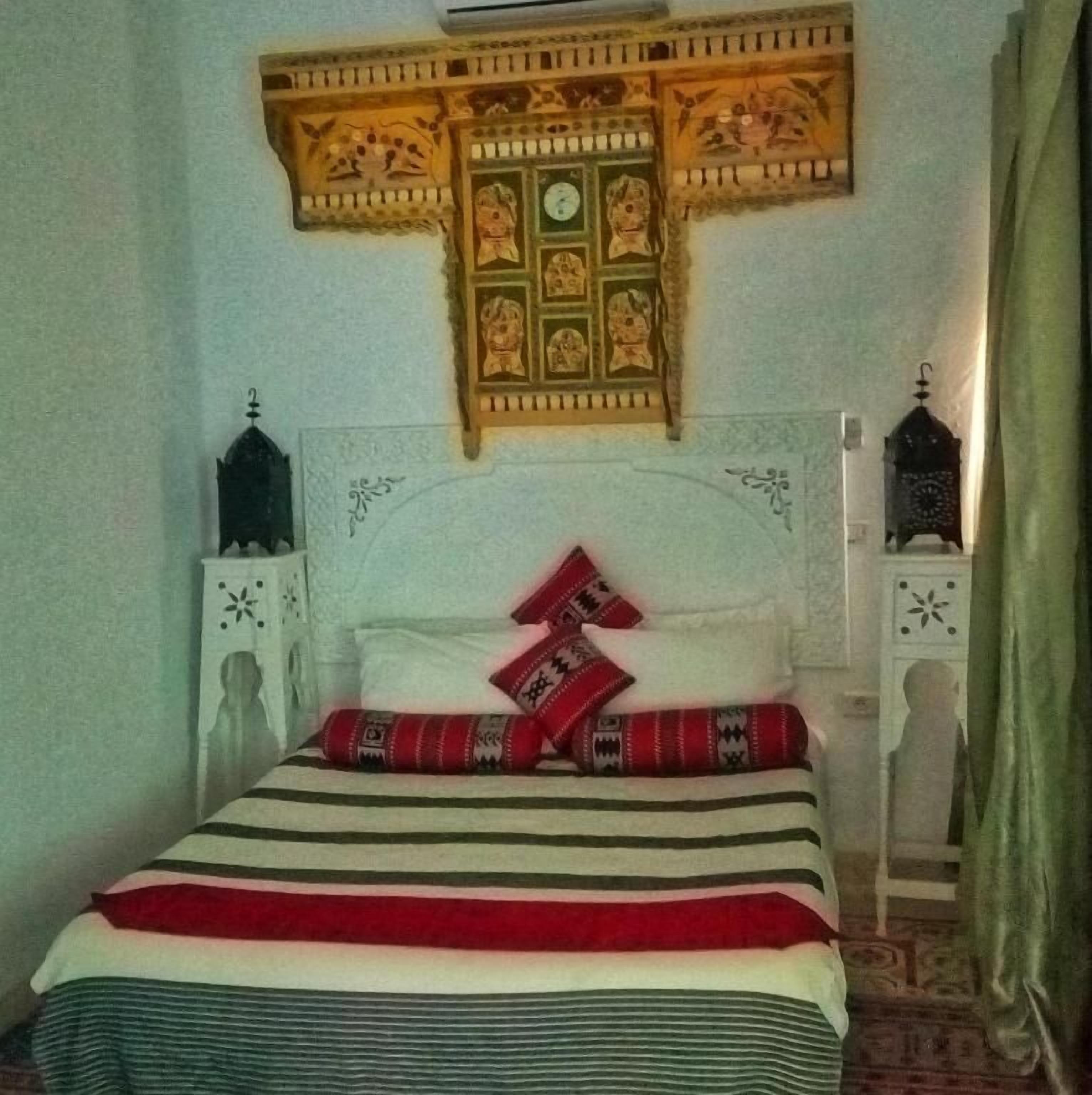 A bed with a white headboard, red and black striped bedding, and a decorative wall hanging above it.